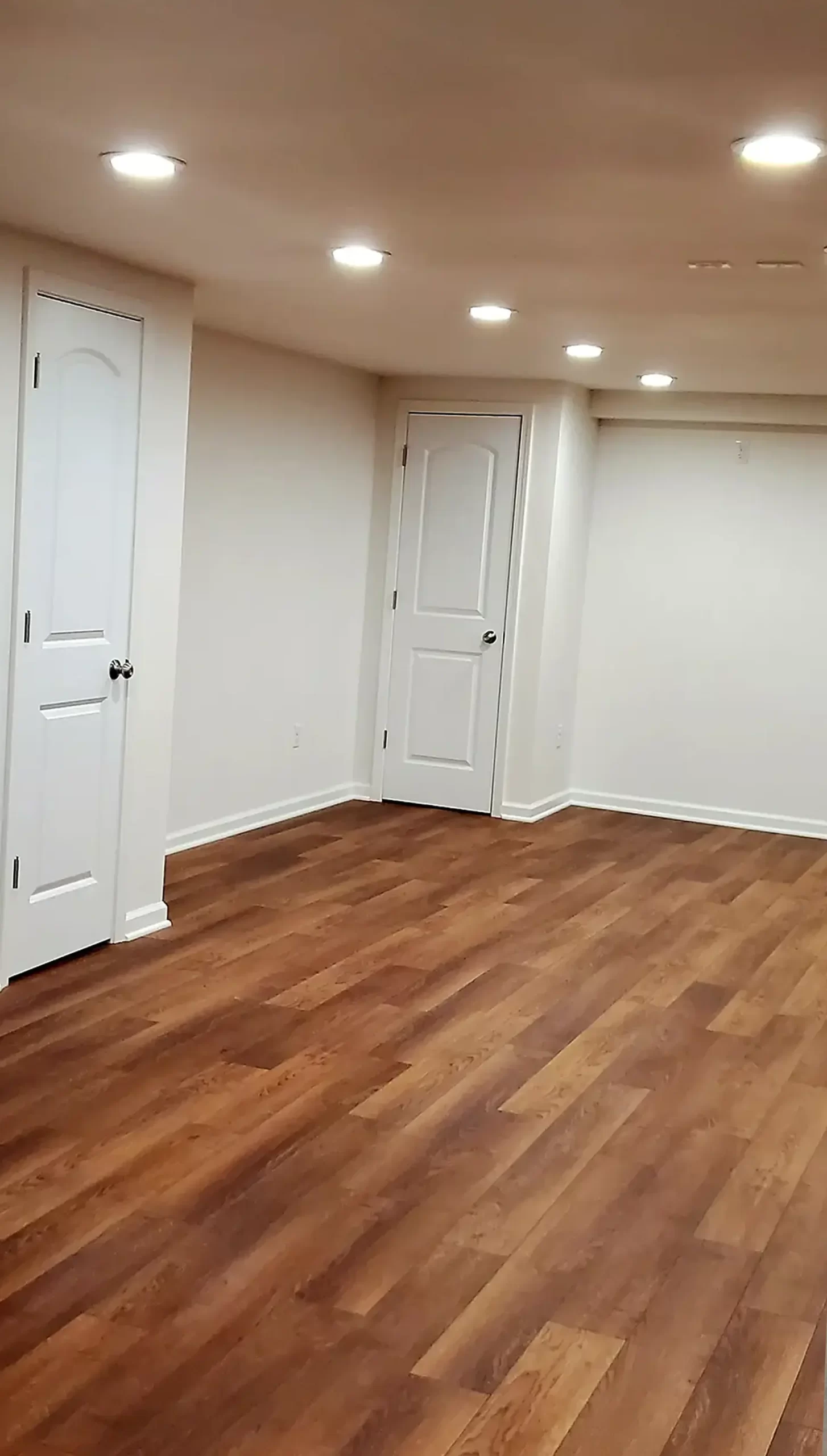 Finished basement with wood-look flooring, drywall, recessed lighting and white trim